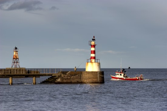 Fishing boat passing Amble Lighthouse on it's way to Amble Harbour, Northumberland.